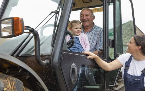 A shot of a grandfather sitting in a tractor with his young granddaughter, he is at his farm in North East, England. The grandfather and the girl's mother are teaching her about the farm.